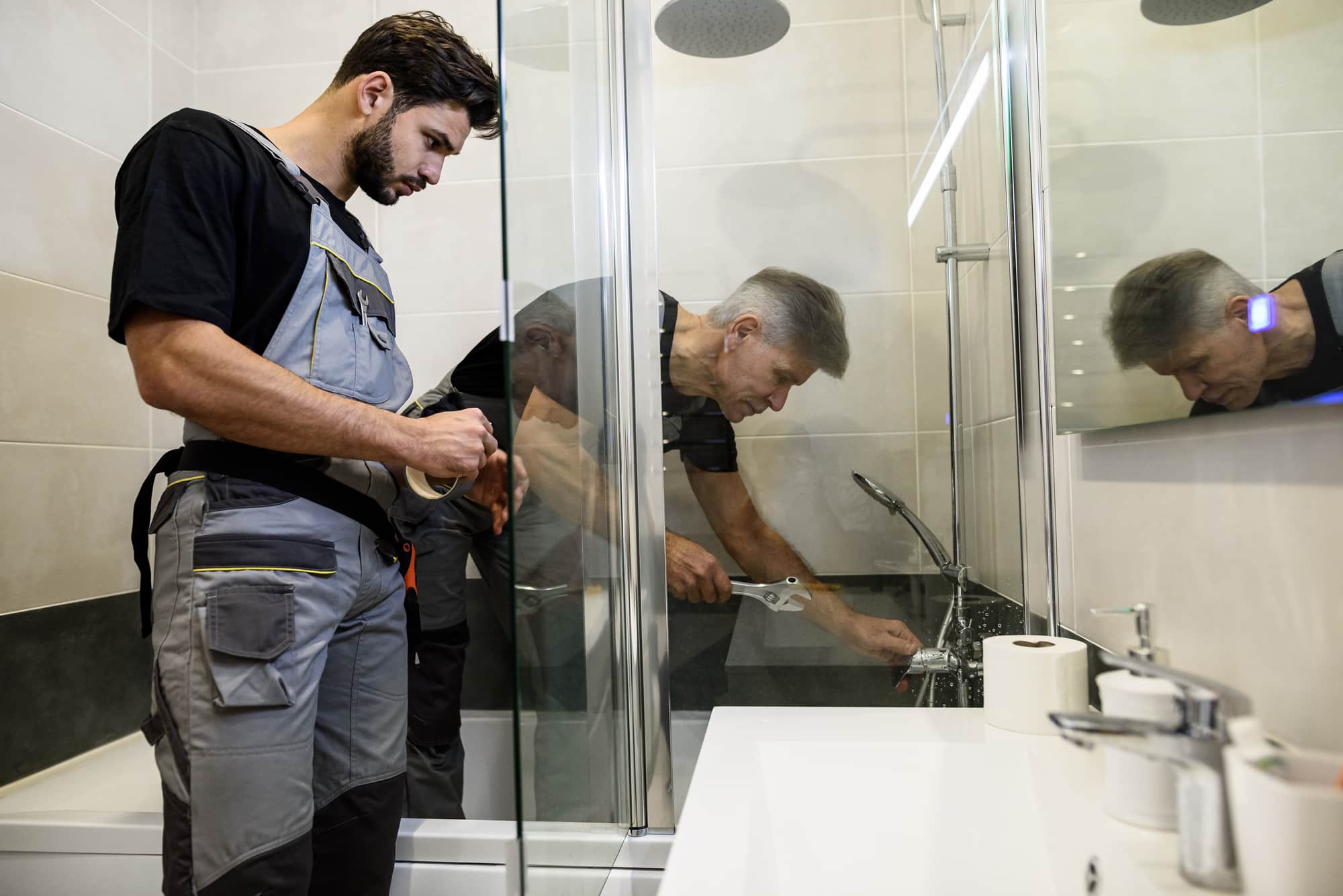 Two plumbers in uniform working, fixing water tap in bathtub