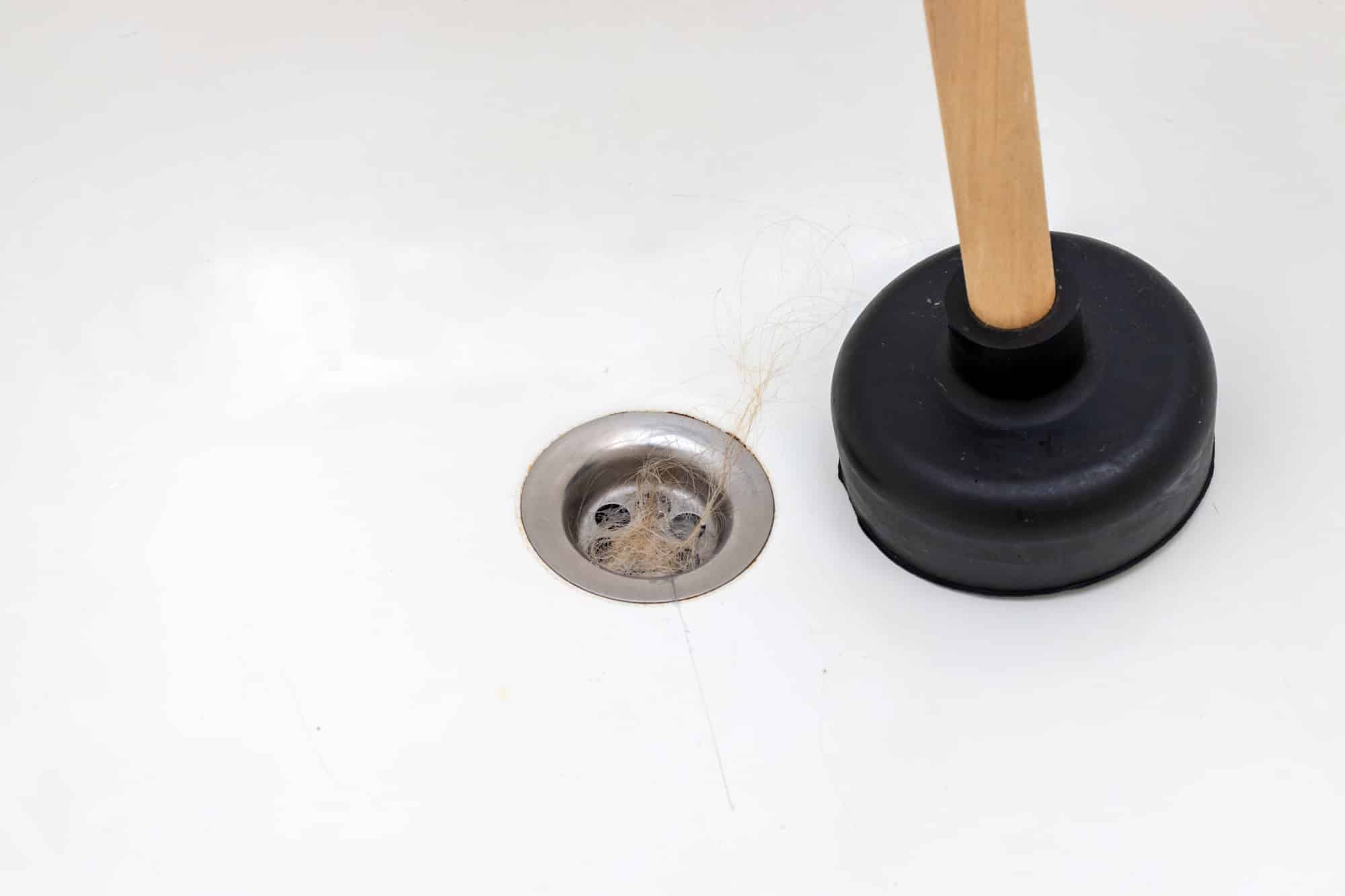 Clogged bath drain with fallen out hair and a plunger